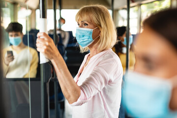 Older female in face mask standing in bus using tissue