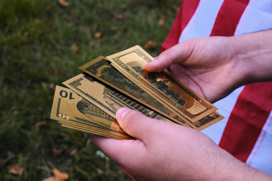 Billetes De Dólar Dorados En Las Manos De Un Hombre Frente A Una Bandera De Estados Unidos