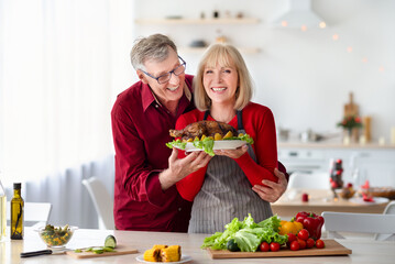 Positive Caucasian senior couple cooking Thanksgiving or Christmas turkey together at kitchen