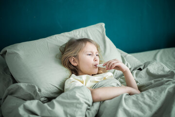 A little girl lies in bed and is sick, feeling unwell and having a cold in the winter