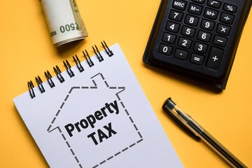 Notepad with the text property tax inside house outline placed on yellow background with Indian currency banknotes and calculator. 