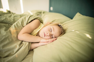 Obraz na płótnie Canvas Little caucasian girl with blond hair sleeps in a soft bed of light green color