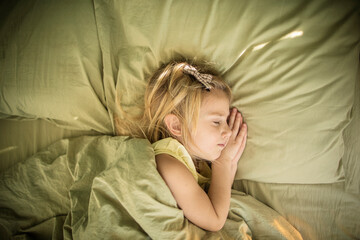 Little caucasian girl with blond hair sleeps in a soft bed of light green color