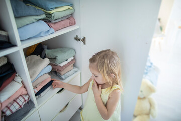 Little caucasian blonde girl neatly folds clothes on her shelf