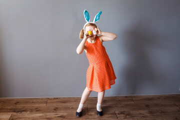 Funny little girl in orange dress and bynny ears closing her eyes with painted Easter eggs.