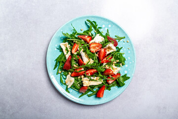 Fresh strawberry salad with arugula, strawberries and cheese brie, camembert. Plate with a keto diet food. Delicious breakfast or snack on a light background, top view