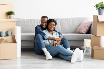 Happy african-american couple sitting in room with cardboard boxes on moving day