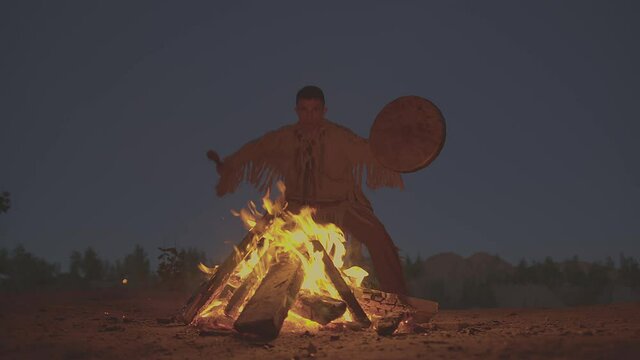 A shaman with a drum jumps in around the fire in clothes for the ceremony.