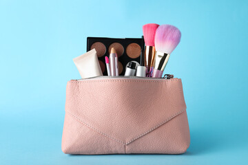 Cosmetic bag with makeup products and accessories on light blue background