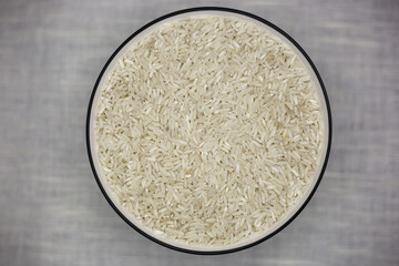 Rice in a white deep plate with a black rim close-up from above on a white textured fabric