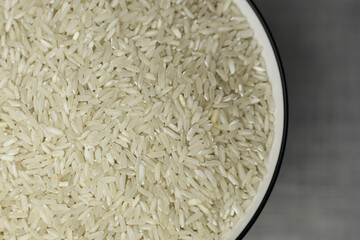 Rice in a white deep plate with a black rim close-up from above on a white textured fabric