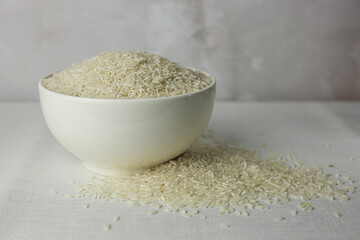Rice in a white deep plate close-up side view on a white textured fabric