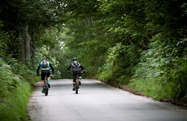 The backs of two mountain bike cyclists riding up a steep road hill, Bale Hill, near Blanchland in County Duram.