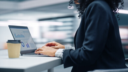 Modern Office: Black Businesswoman Sitting at Her Desk Working on a Laptop Computer. Successful African American Woman working with Big Data e-Commerce. Motion Blur Background