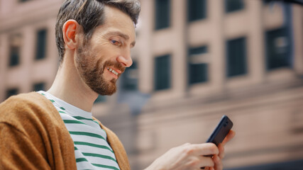 Street Shot: Portrait of Caucasian Man Using Smartphone in the Big City. Creative Professional Using Mobile Phone App for e-Commerce Online Shopping. Blurred Background.