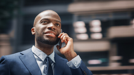 Street Shot: Portrait of Happy Black Businessman Talking on Smartphone in City. Successful African...