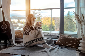 Woman in knitted wool sweater drinks tea a cup, relax at home in winter day. Health care,...
