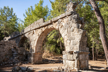 Fototapeta na wymiar Ruins of the aqueduct of the ancient ancient city of Phaselis illuminated by the bright sun in Pine forest, woods in sunny weather in Turkey, Antalya, Kemer. Turkey national nature landmarks.
