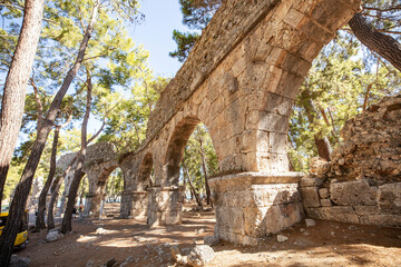 Ruins of the aqueduct of the ancient ancient city of Phaselis illuminated by the bright sun in Pine forest, woods in sunny weather in Turkey, Antalya, Kemer. Turkey national nature landmarks.