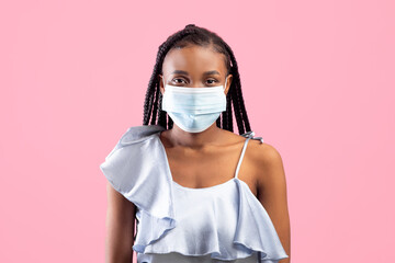 Coronavirus protection. Young black woman in protective medical face mask looking at camera on pink...