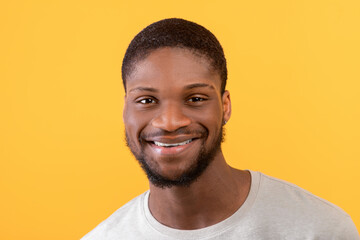 Fototapeta premium Closeup portrait of young african american man smiling at camera, standing isolated over yellow background, free space