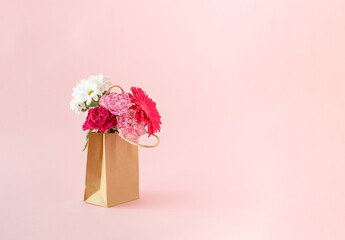 Fresh flowers in bloom packed in a brown paper bag on a pink background. Minimal concept.