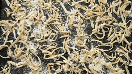 Strips of homemade noodles are dried on a baking sheet sprinkled with flour. Close-up, top view, healthy eating concept..