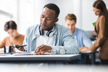 Black man sitting at desk writing exam, reading tasks