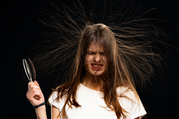 Woman with long static electric hair stand on ends and a brush in hand, on black background.