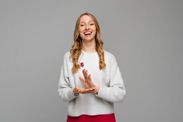 young pretty woman feeling happy and successful, smiling and clapping hands, saying congratulations with an applause, wears white sweater, standing over gray background