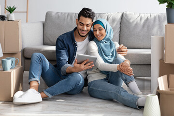 Loving muslim family sitting on floor with tablet among boxes
