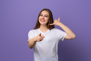 Young beautiful brunette girl wearing white t shirt standing over purple background smiling doing...