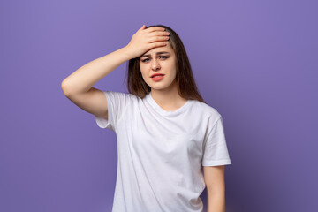 Cute girl remembered something and holding his head. Portrait of a stressed woman, standing in blank white t shirt over purple background