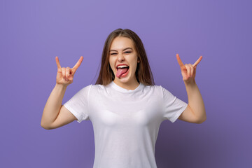 Excited carefree brunette girl in blank white t shirt, having fun at awesome student party, show tongue and smiling, make rock n roll gesture to express excitement