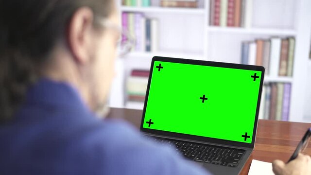 Over the shoulder shot of a man working looking at green screen. Office person using laptop computer with green screen.