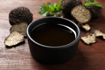 Fresh truffle oil in bowl on wooden table, closeup
