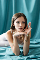 sensual tattooed woman with white tiny flowers on body looking away while lying on green cloth.