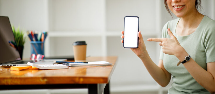 A smiling woman holds a smartphone in his hands, Mockup image of a beautiful woman pointing finger at a mobile phone with blank white screen
