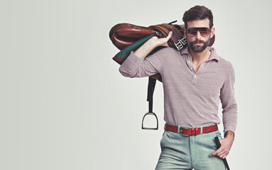 Wanna go for a ride. Studio shot of an attractive man in retro 70s wear holding a saddle and riding crop.