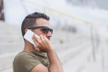 Happy man in sunglasses standing outdoors, talking by smartphone