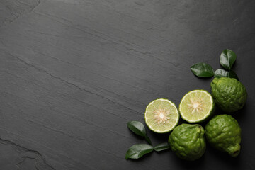 Fresh ripe bergamot fruits with green leaves on black table, flat lay. Space for text