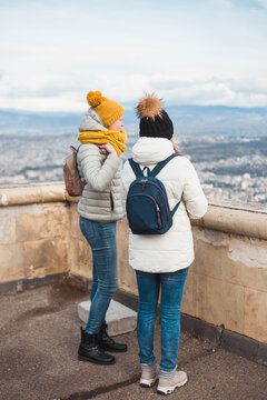 Two women inspect the city from a high observation deck - tourists on a journey in the Caucasus in winter