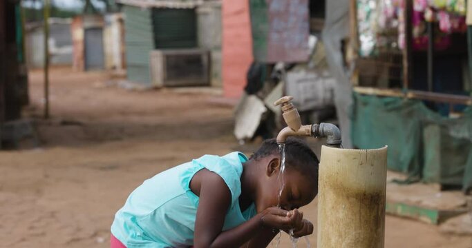 Poverty.Inequality.Poor black african girl drinking water from a communal faucet in an informal settlement slum
