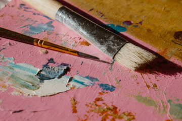 Painting brush and palette knife, bright background with paint strokes.