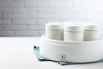 Modern yogurt maker with full jars on white wooden table. Space for text