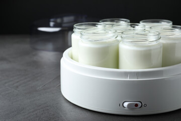 Modern yogurt maker with full jars on grey table. Space for text