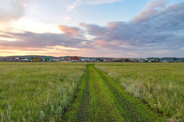 Fototapeta na wymiar Dirt road leading to the village in summer on the background of sunset