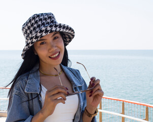 Beautiful asian woman holding black eyeglasses with hat on the sea