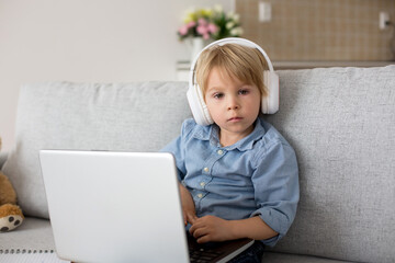 Sweet blond child, boy in casual clothes, woring on computed at home