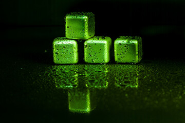 Green stainless steel cubes simulating ice for cooling drinks on a black surface with a reflection.